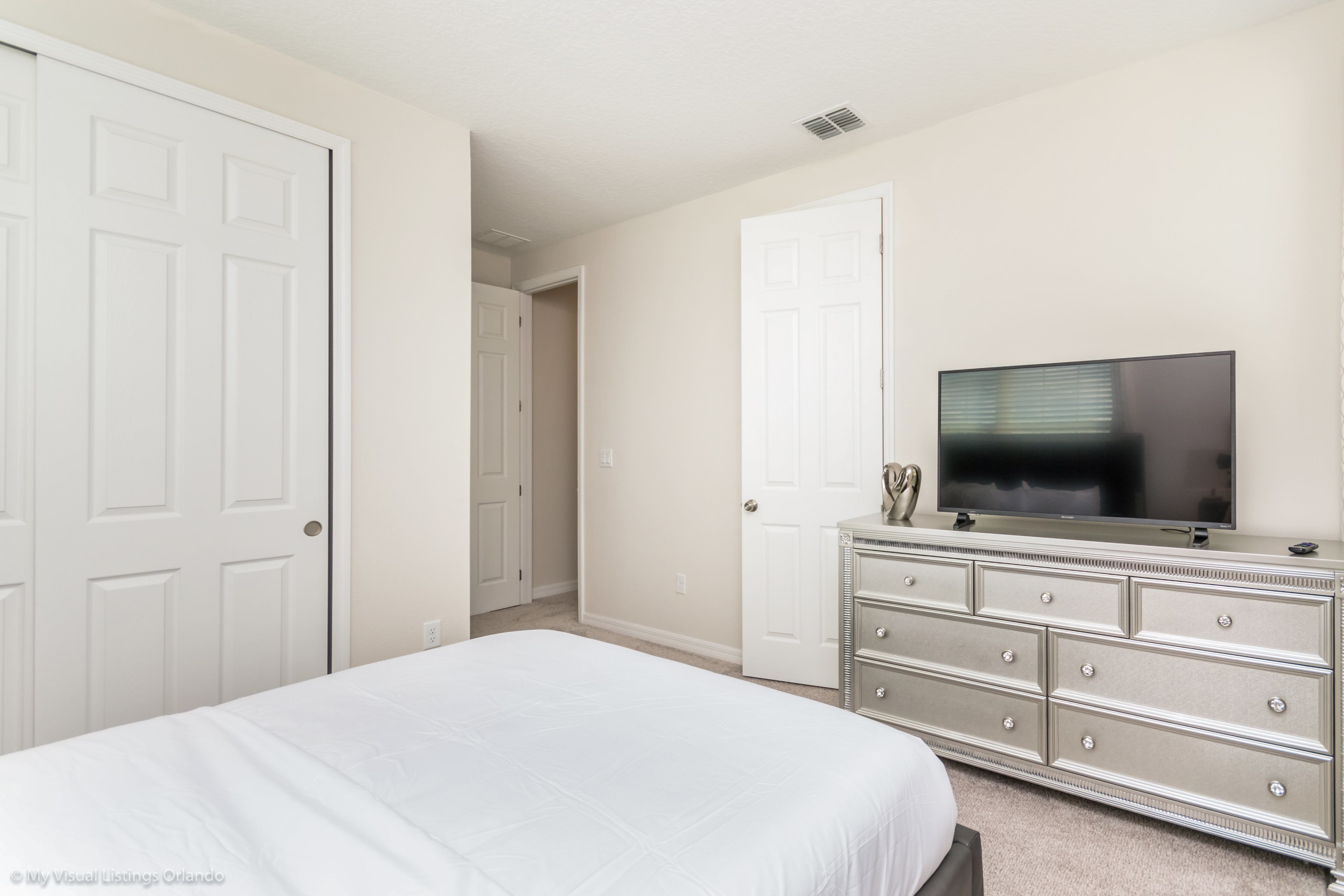 A bedroom with a bed, a dresser, a television, and two doors.