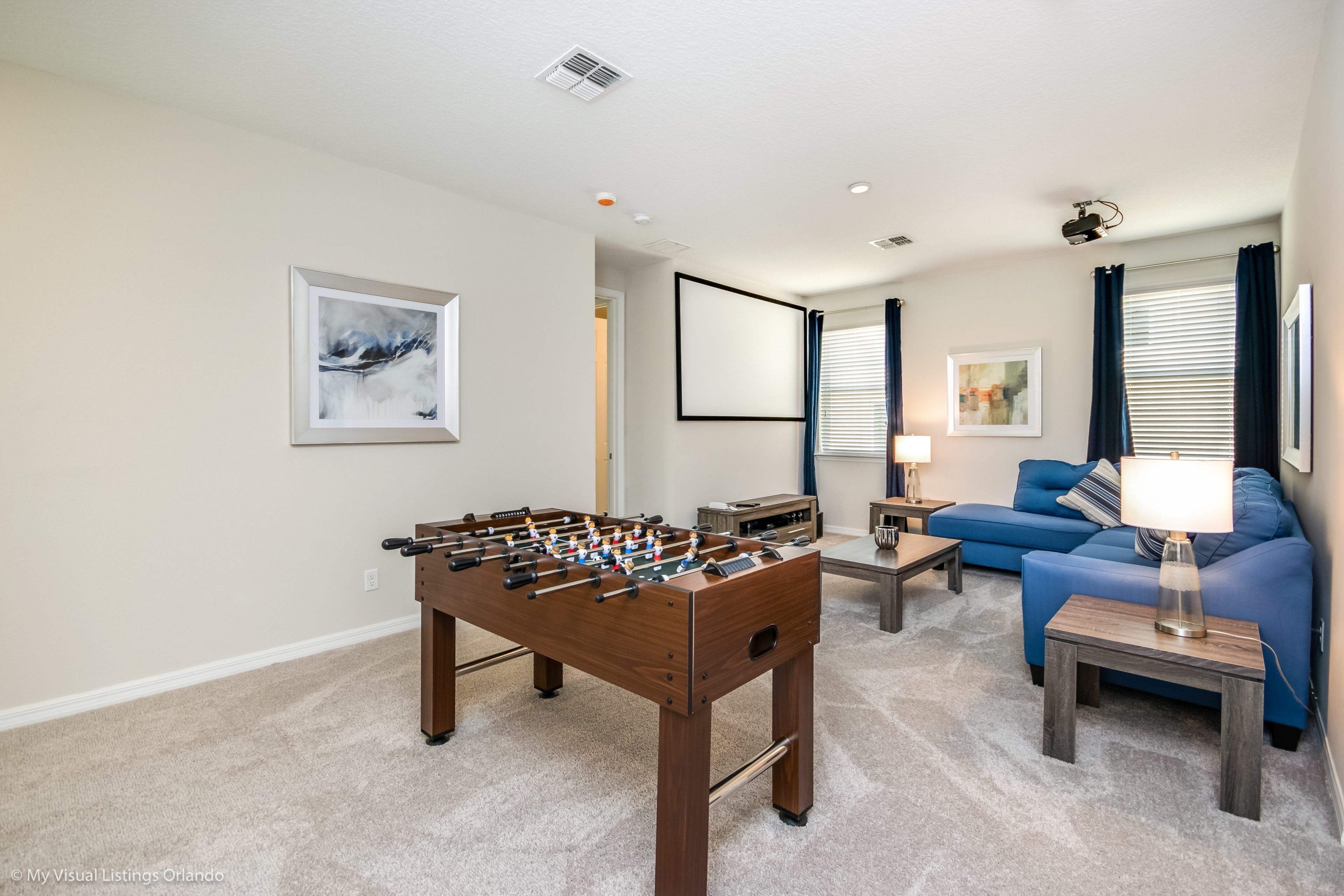 A living room with a foosball table, a blue sofa, and a lamp.