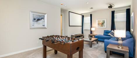 A living room with a foosball table, a blue sofa, and a lamp.