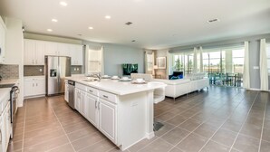 A spacious kitchen with white cabinets, a large island, and a dining area with a white sofa and table.