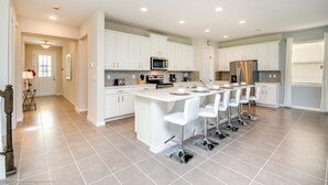 A modern kitchen with white cabinets, a central island with bar stools, a microwave, and a refrigerator.