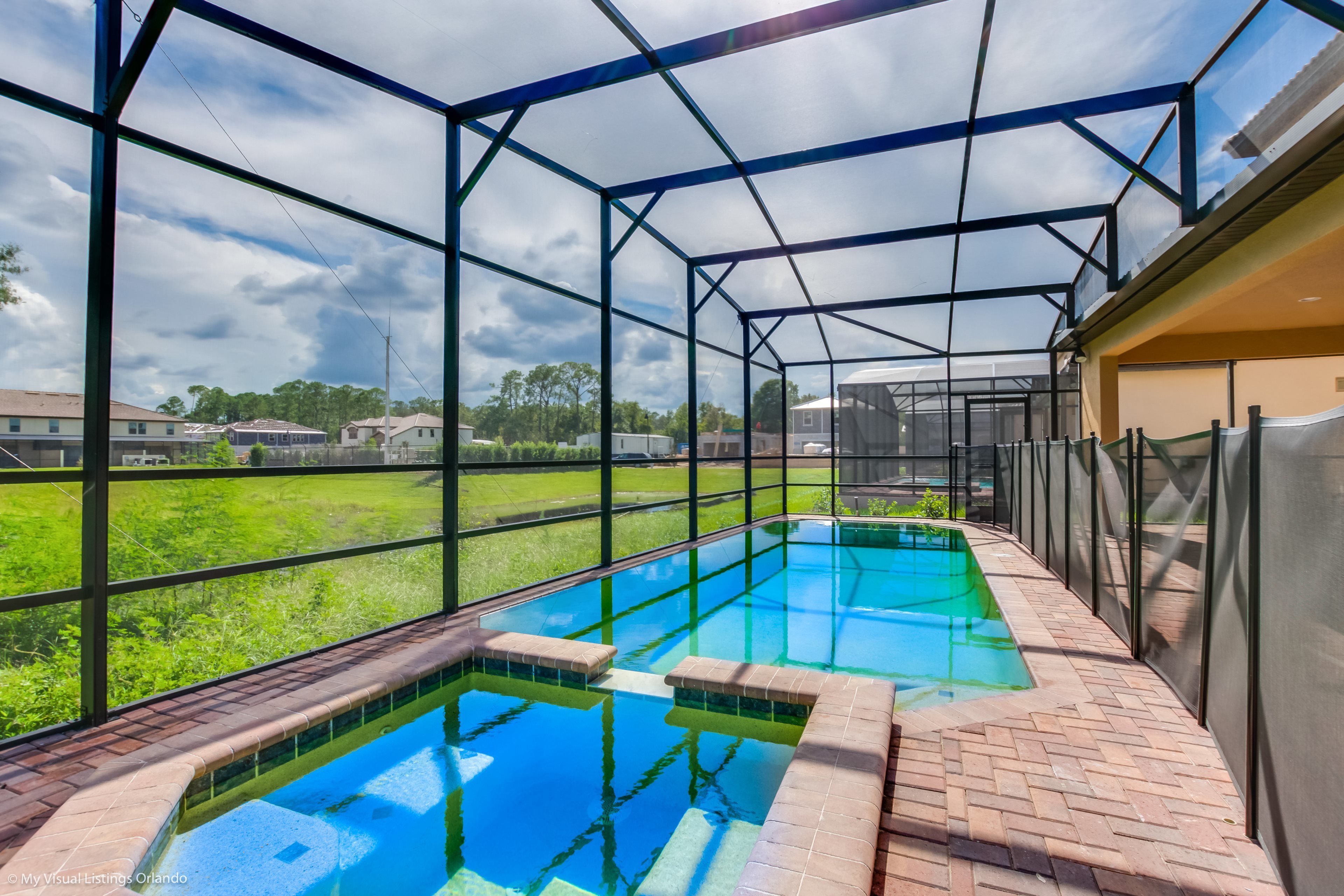 A covered swimming pool with clear glass walls and a brick border, surrounded by a metal frame structure.