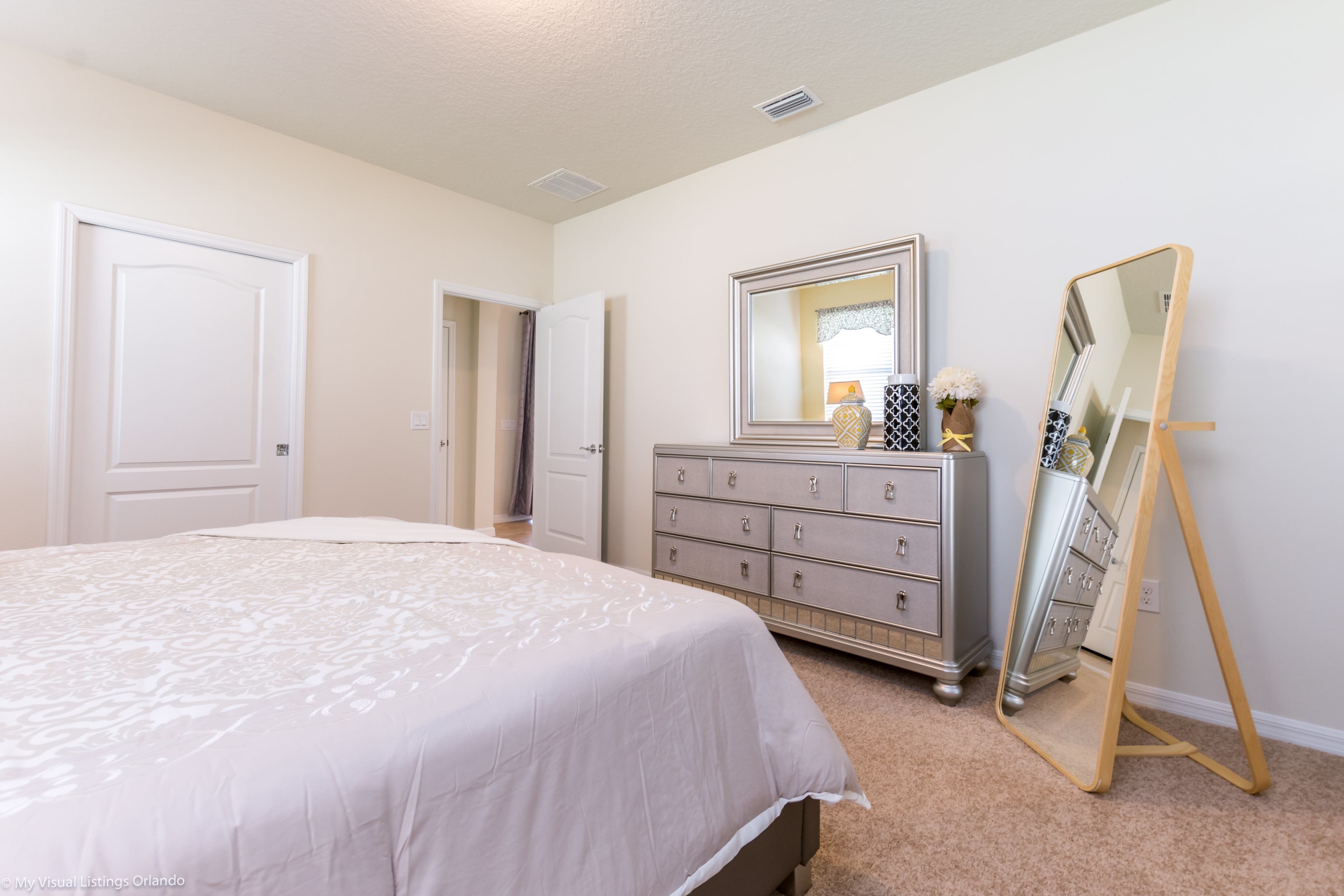 A bedroom with a bed, dresser, and a full-length mirror.