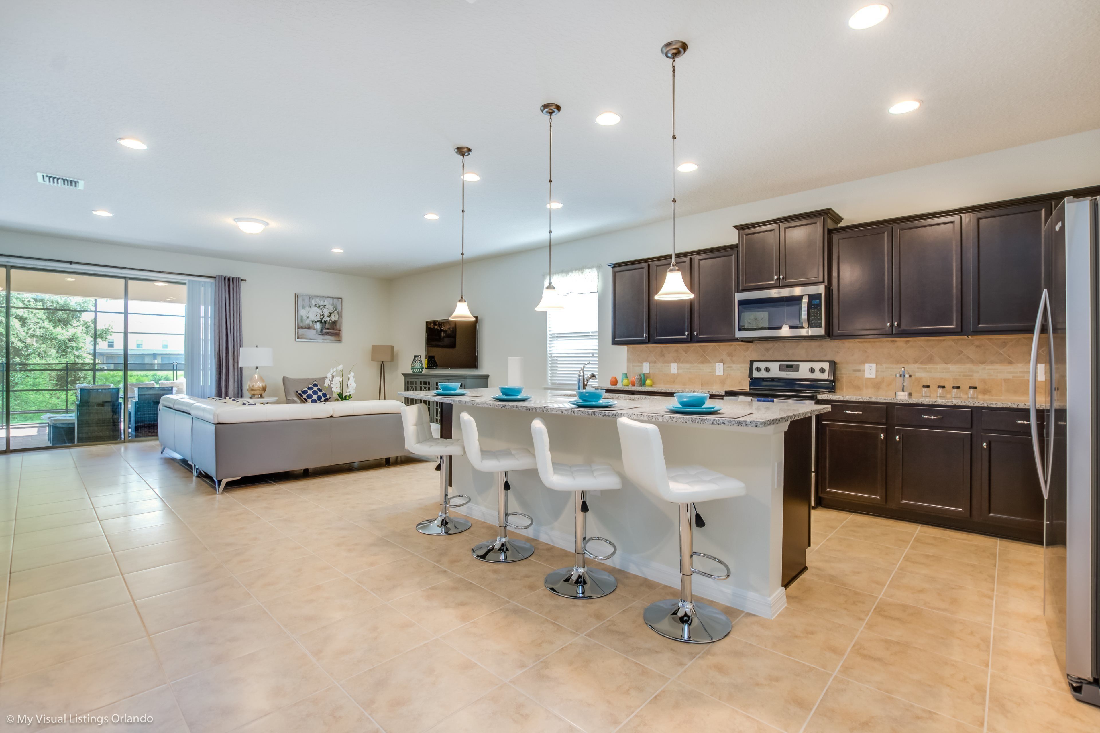 A modern kitchen with dark cabinets, a central island with bar stools, a microwave, and a refrigerator.