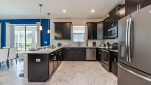 A modern kitchen with dark cabinetry, stainless steel appliances, and a marble floor.