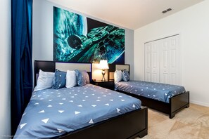 Un dormitorio con dos camas, una obra de arte grande en la pared, una mesita de noche con una lámpara y una puerta blanca.