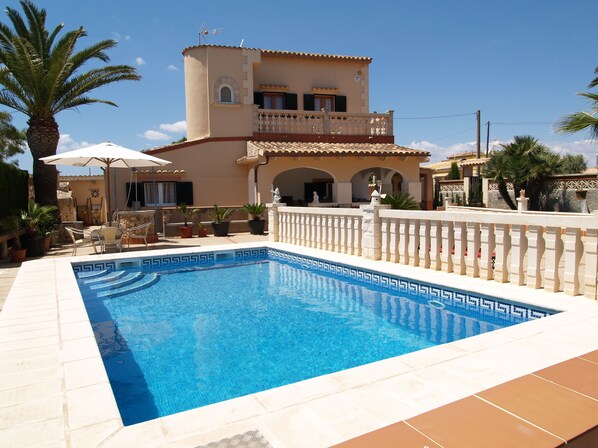 Una piscina con un diseño geométrico de mosaicos, rodeada por una cerca blanca y un edificio color beige con un balcón.