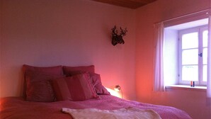 Un dormitorio con cama, almohadas, una colcha, una decoración de cabeza de ciervo en la pared y una ventana con cortinas.
