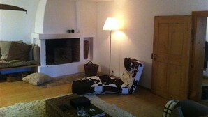 Una sala de estar acogedora con chimenea, un sofá, un sillón estampado y una lámpara.
