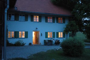 A two-story house with a red-tiled roof, green shutters, and a gravel driveway. - Der Hanselhof (Ruderatshofen)