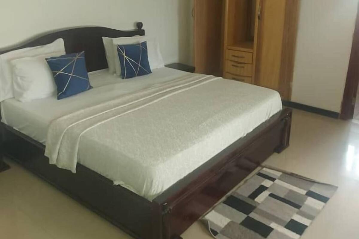 Une chambre à coucher avec un lit, des oreillers, une armoire en bois et un sol carrelé.