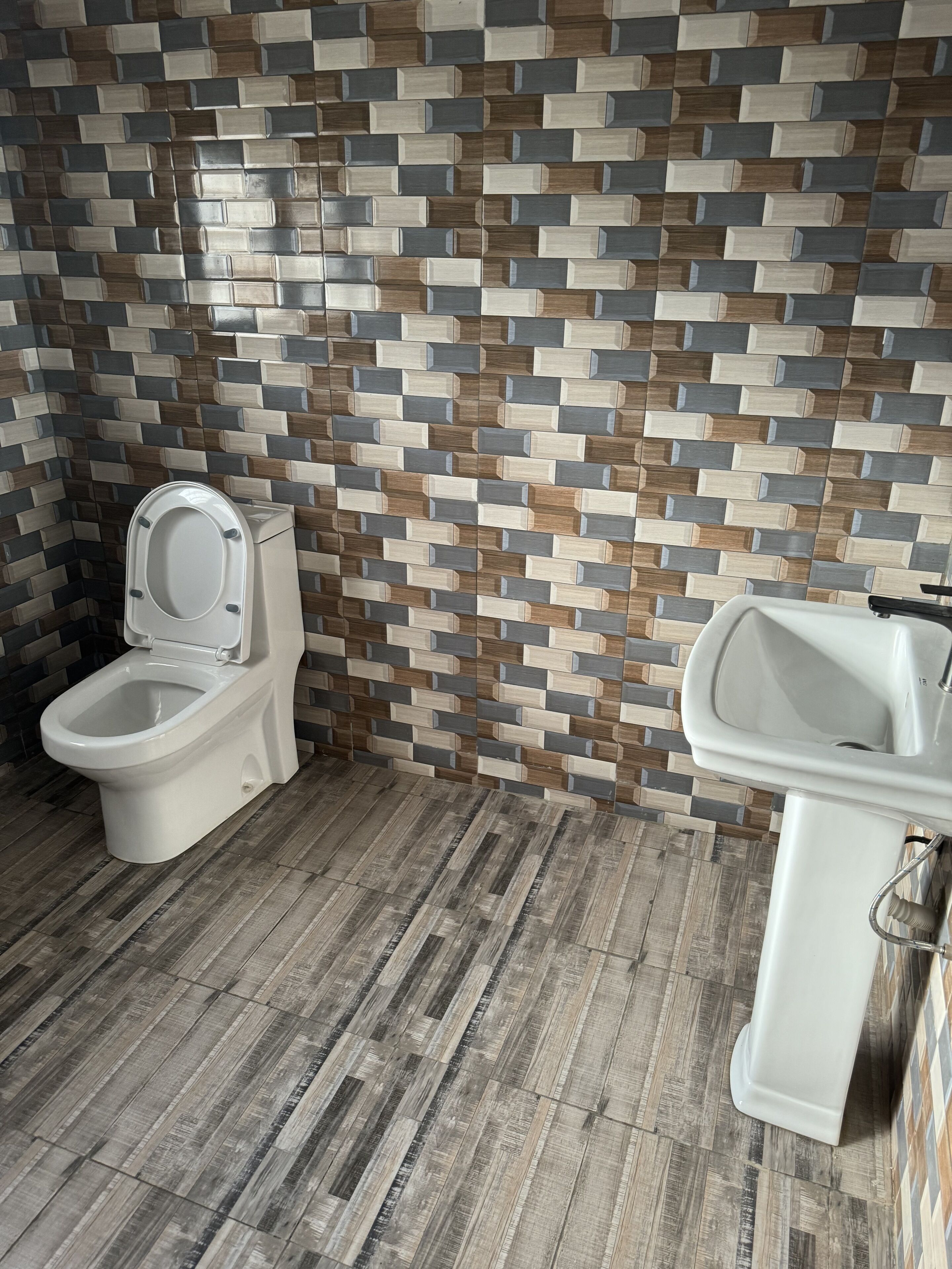 Ein Badezimmer mit Toilette und Waschbecken, Holzboden und einer Wand mit Musterfliesen.