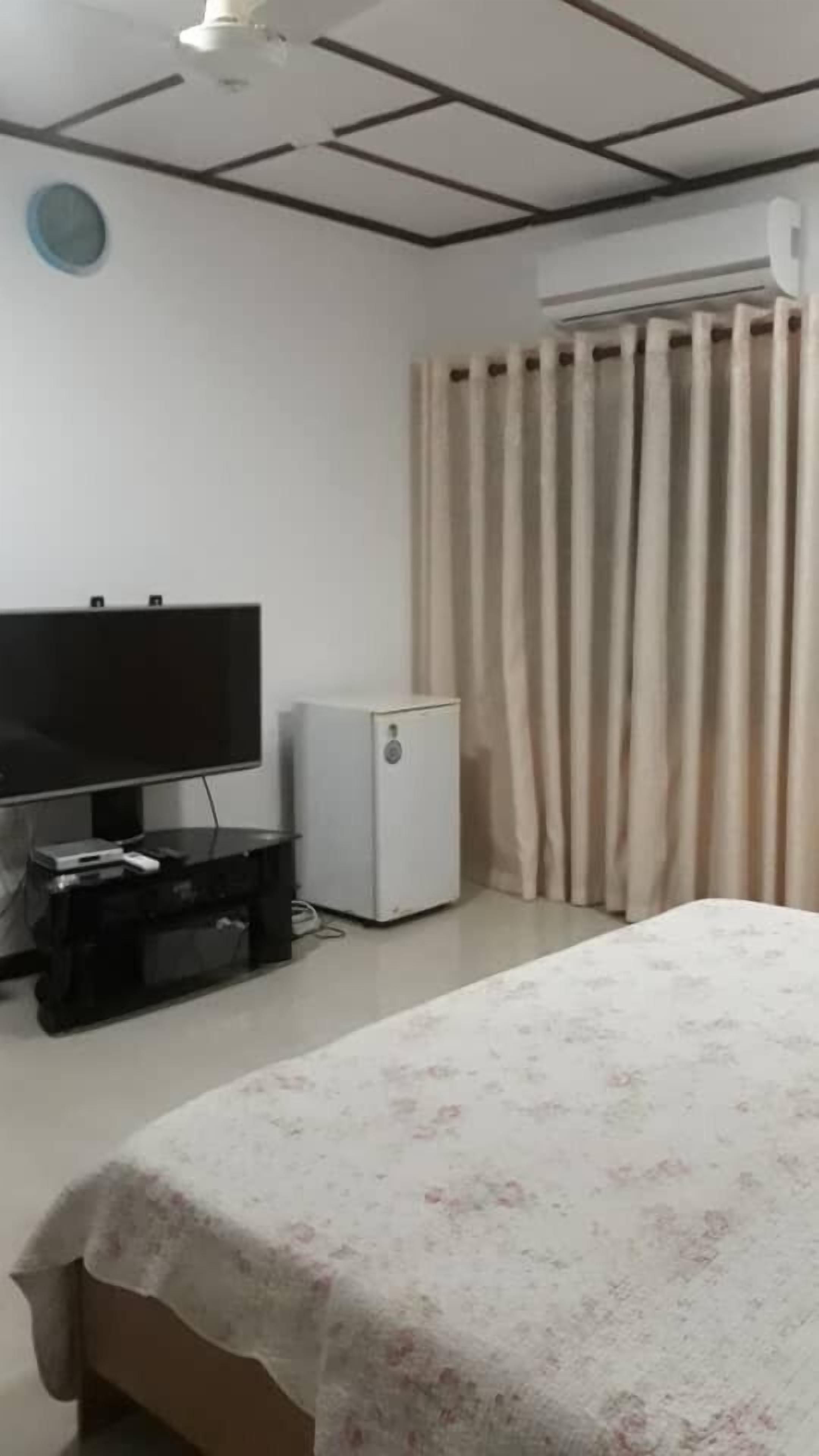 Een hotelkamer met een bed, een televisie, een kleine koelkast en een raam met gordijnen.
