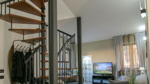 Un salon avec un escalier, un téléviseur à écran plat, un canapé et une fenêtre avec des rideaux.