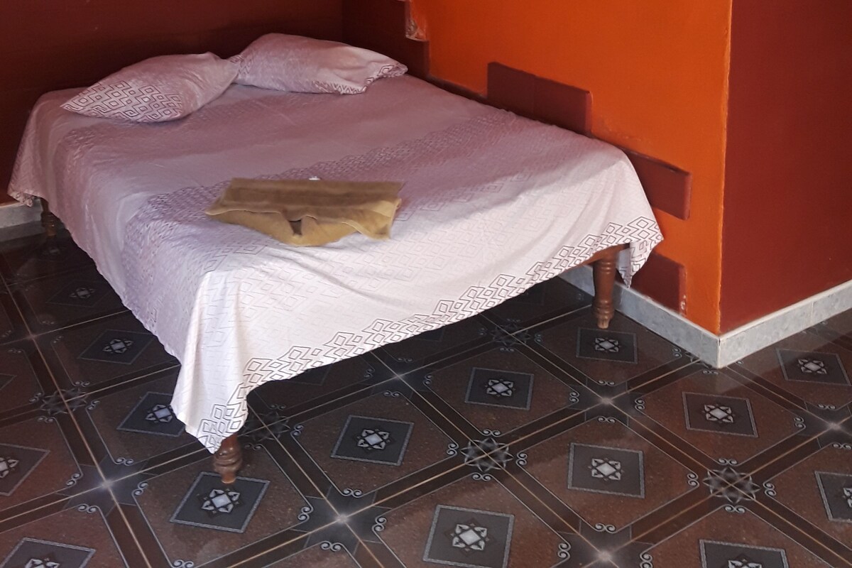 A room with a bed, orange walls, and patterned floor tiles.