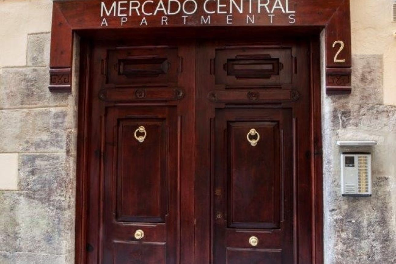 A double wooden door with a brass handle and a sign above reading "Mercado Central Apartments".