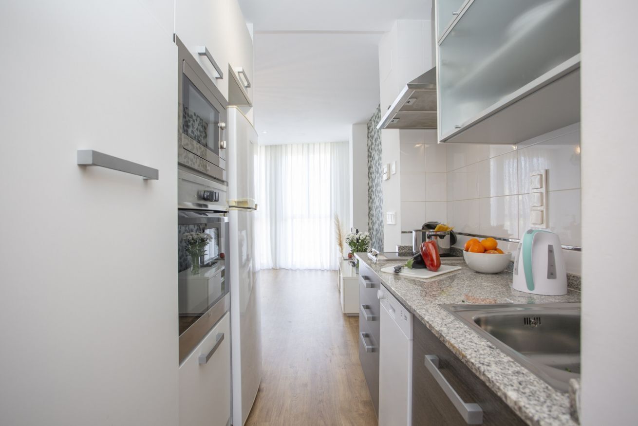 Una cocina moderna con muebles blancos, electrodomésticos de acero inoxidable y encimera de granito.