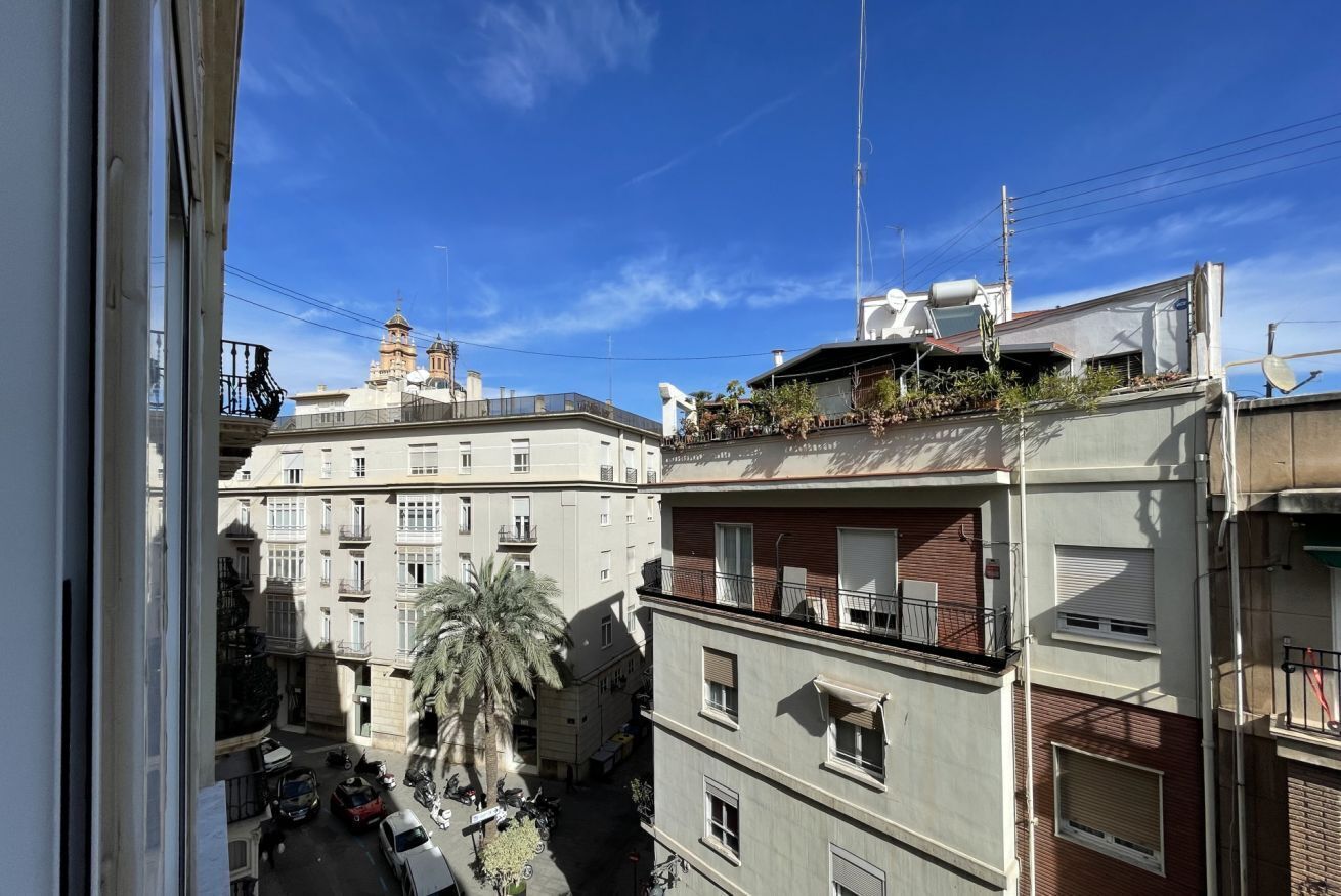Un edificio de varios pisos con balcones, una palmera y un cielo azul despejado.