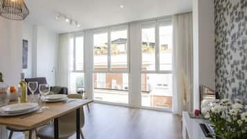Un comedor moderno con una mesa de madera preparada para dos, ventanas amplias con cortinas y vistas al exterior.