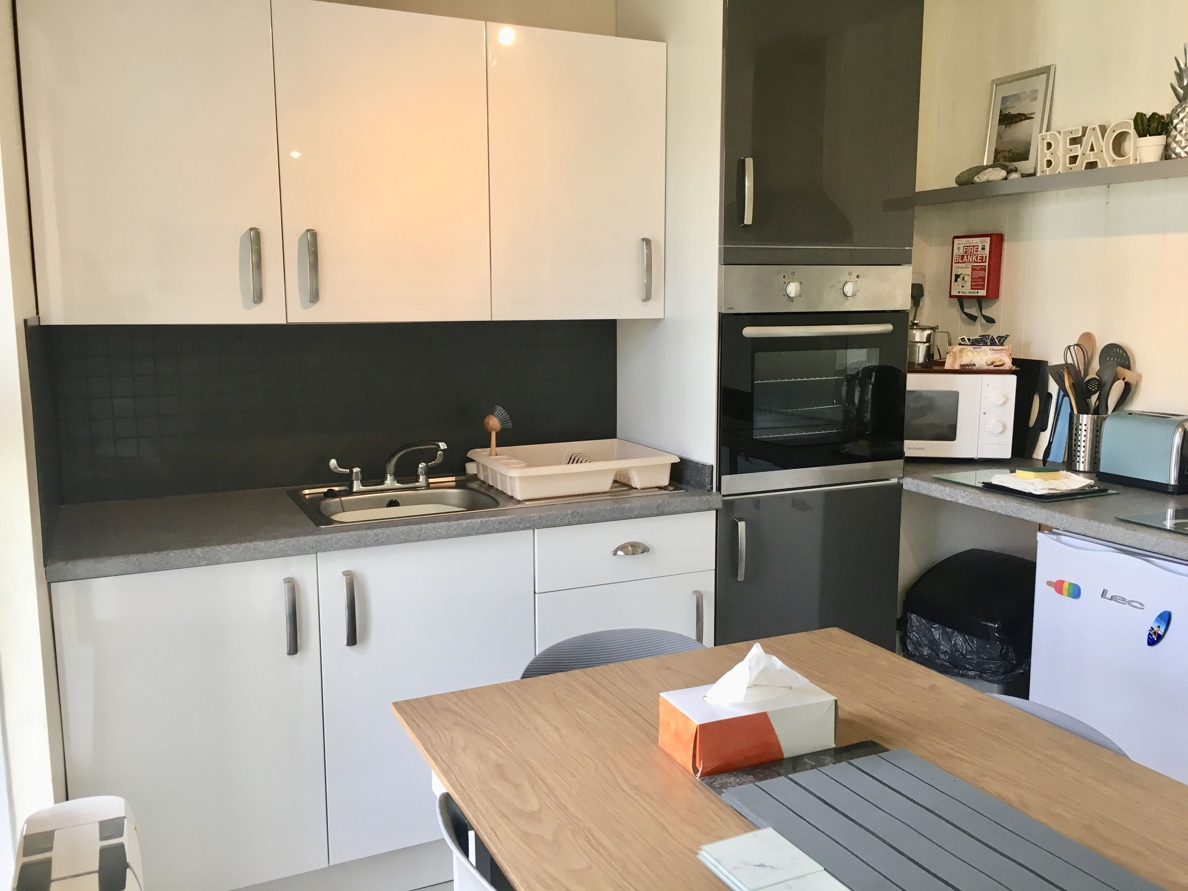 A modern kitchen with white cabinets, a double sink, a microwave, an oven, and a toaster.