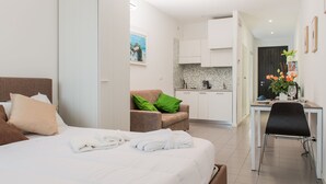 Una habitación de hotel moderna con una cama grande, una zona de estar con una silla, un escritorio y una kitchenette.