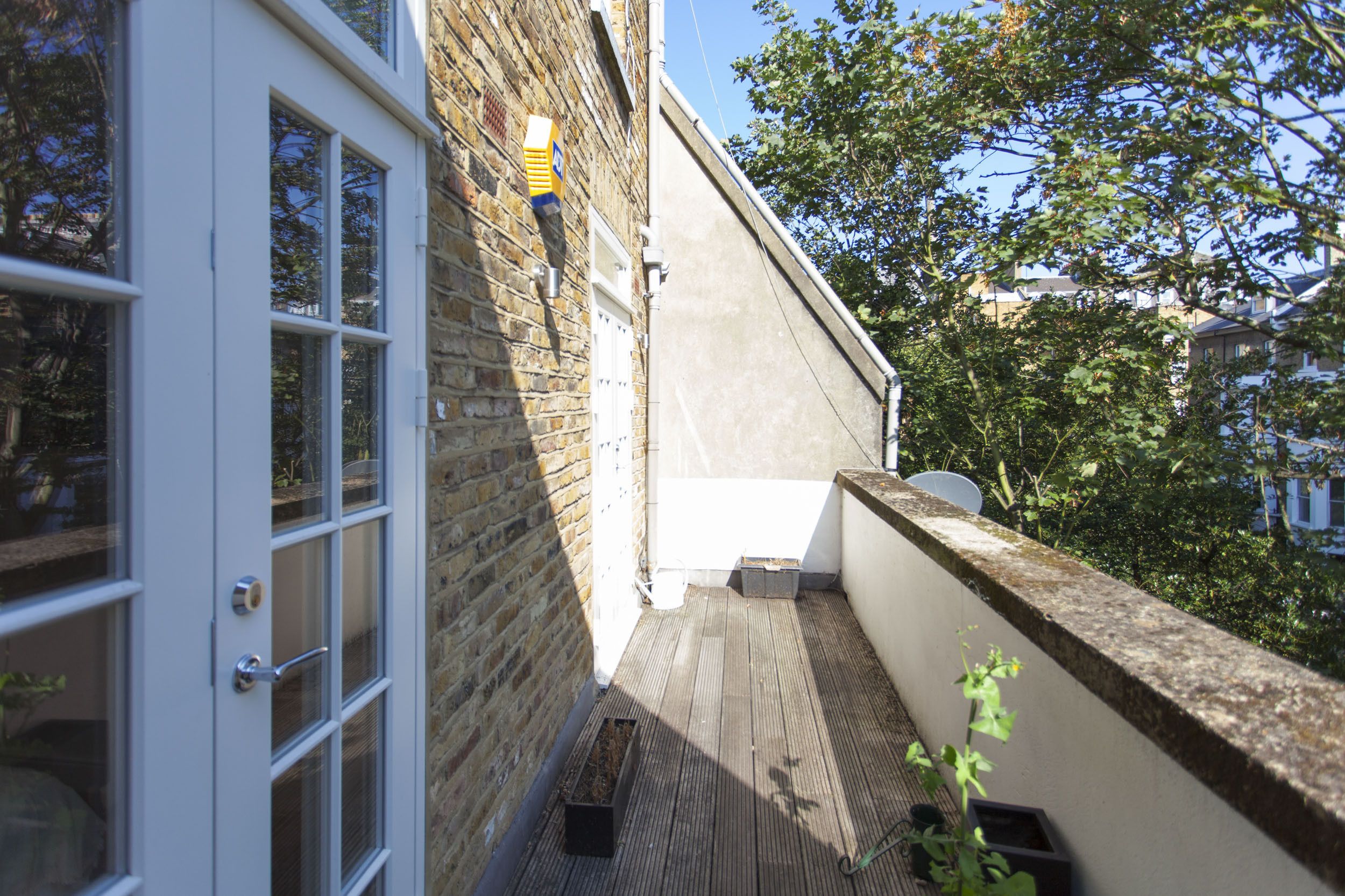 A narrow outdoor corridor with a wooden floor, a white door, and a brick wall.