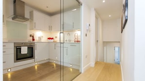 A modern kitchen with white cabinets, a glass partition, and a wooden floor. - Chelsea Residential Atmosphere (London)