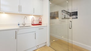 A modern kitchen with white cabinets, a stainless steel sink, and a glass door leading to a hallway. - Chelsea Residential Atmosphere (London)