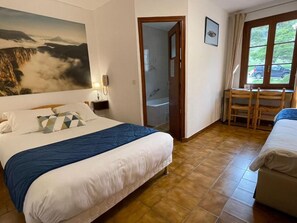 Un dormitorio con cama, escritorio con sillas, baño y un ventanal grande.