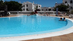 Una piscina con solárium de baldosas, rodeada de edificios blancos con ventanas de arco y techos abovedados.