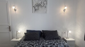 Un dormitorio con una colcha de lunares, dos almohadas, una toalla roja y dos lámparas de noche.