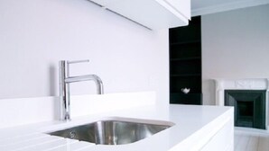 Uma cozinha moderna com pia de aço inoxidável, bancadas brancas e painel de fundo preto.