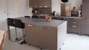 A modern kitchen with a central island, bar stools, a microwave, and a coffee maker. - VILLA WITH HEATED SWIMMING POOL / HOUSE WITH HEATED POOL (Lège-Cap-Ferret)