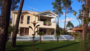 A two-story house with a balcony, surrounded by trees and a well-maintained lawn. - VILLA WITH HEATED SWIMMING POOL / HOUSE WITH HEATED POOL (Lège-Cap-Ferret)