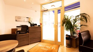 A hotel reception area with a reception desk, a seating area, and a large potted plant. - Le Theatre (Suresnes)
