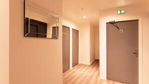 A hallway with wooden flooring, a mirror on the left, and doors with numbers. - Le Theatre (Suresnes)