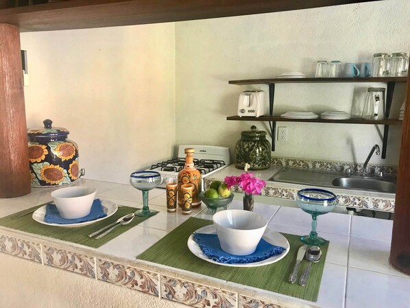 A kitchen with a gas stove, a sink, and a shelf with glassware.