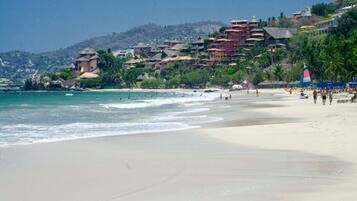 A beach with a clear view of the ocean, a sandy shore, and buildings in the background.