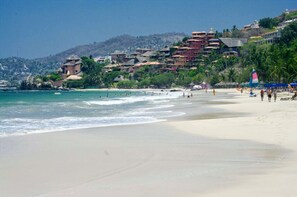 A beach with a clear view of the ocean, a sandy shore, and buildings in the background.