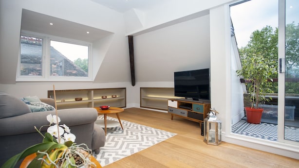 A modern living room with a sofa, TV, wooden flooring, and a large window with a view.
