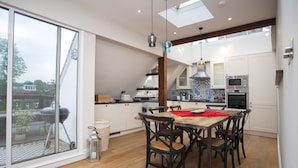 A modern kitchen with white cabinets, a wooden dining table, and a large window overlooking a garden.