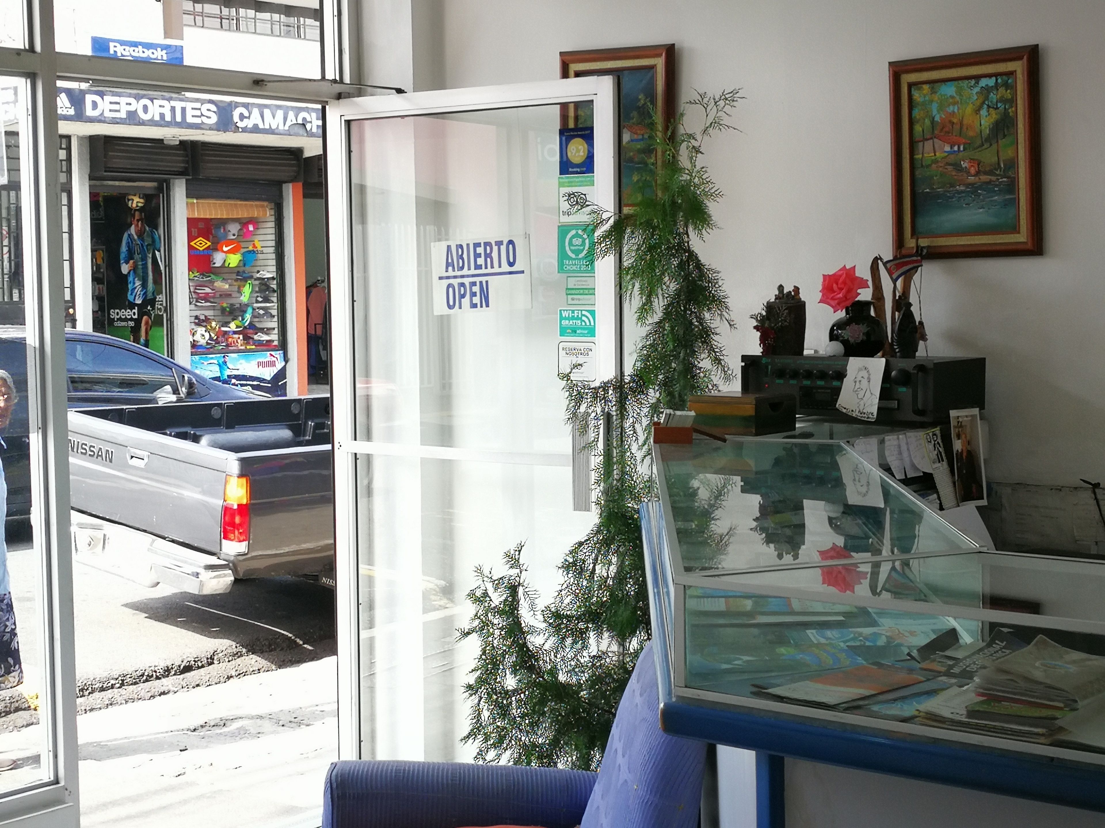 A reception area with a glass counter, a sign indicating the establishment is open, and a Nissan truck parked outside.