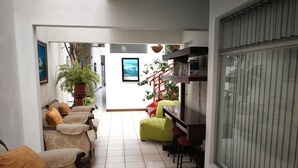 Uma sala de estar com sofá, cadeiras, uma poltrona verde, estante de livros e um vaso com planta.