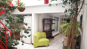 Um quarto amplo e iluminado, com uma escada vermelha, uma poltrona verde e vários vasos de plantas.