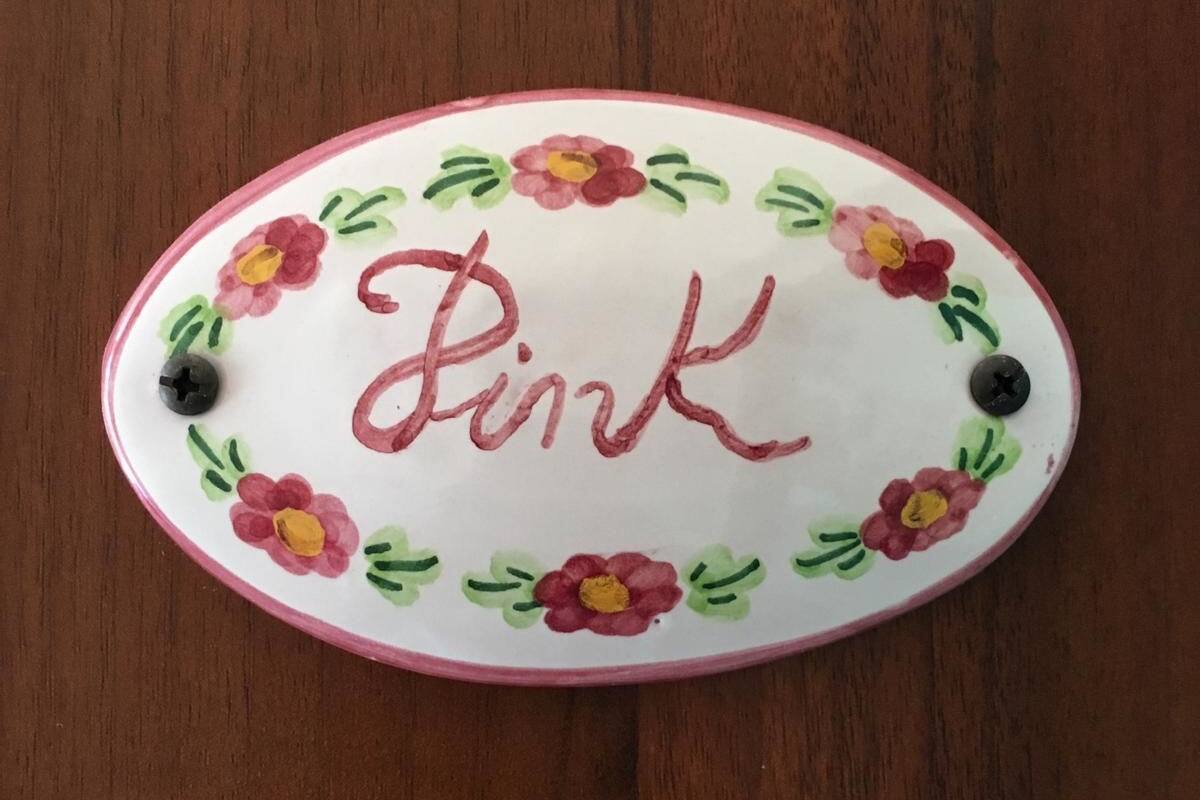 An oval-shaped object with the word "Pink" written in the center, surrounded by floral designs and two black buttons.