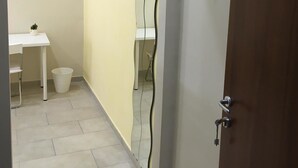 Un corridoio stretto con una scrivania bianca, un piccolo cestino e una porta sulla destra.