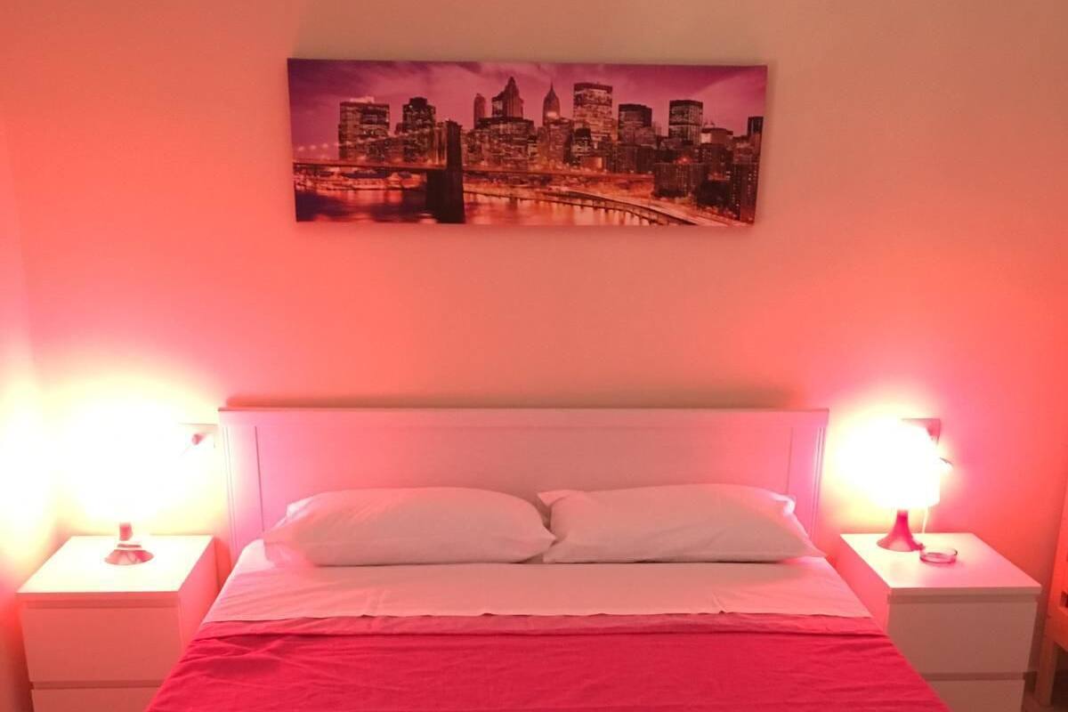A bed with a pink bedspread, two bedside lamps, and a cityscape painting above the bed.