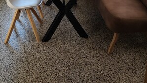 Ruokailutila, jossa on puinen pöytä, valkoiset tuolit, ruskea sohva, hummerin kuva ja lamppu puisen jalustan päällä.