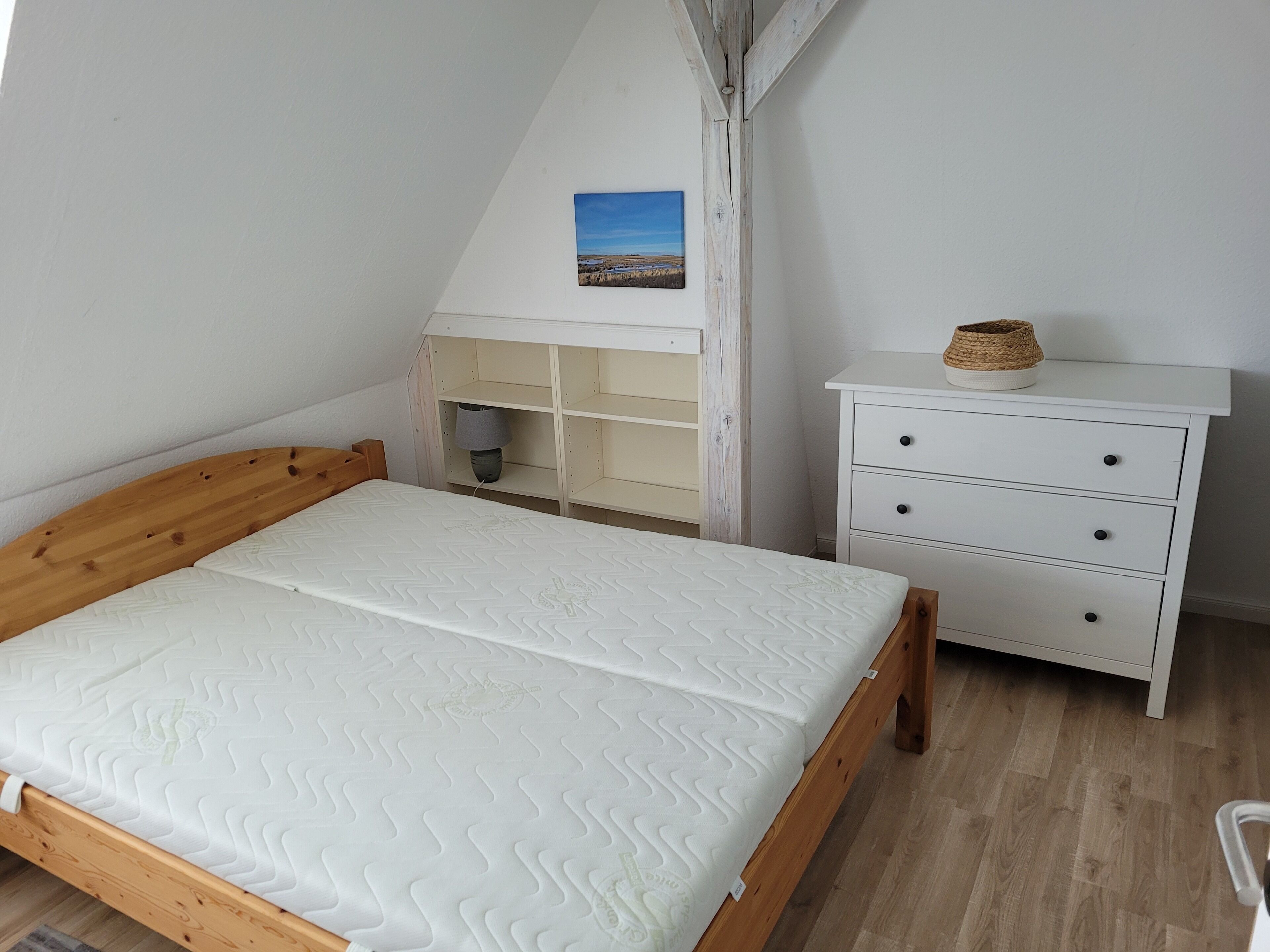 A bedroom with a wooden bed, a white dresser, and a shelf unit with a lamp.