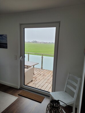 Quarto com porta de correr de vidro que dá para um alpendre ao ar livre, com vista para um campo verde e edifícios distantes.